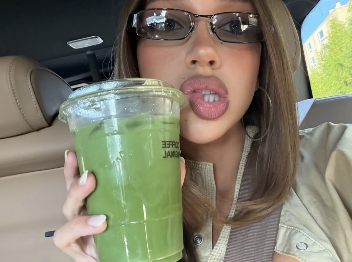 A woman holding a green juice in a candid, modern clean-girl image