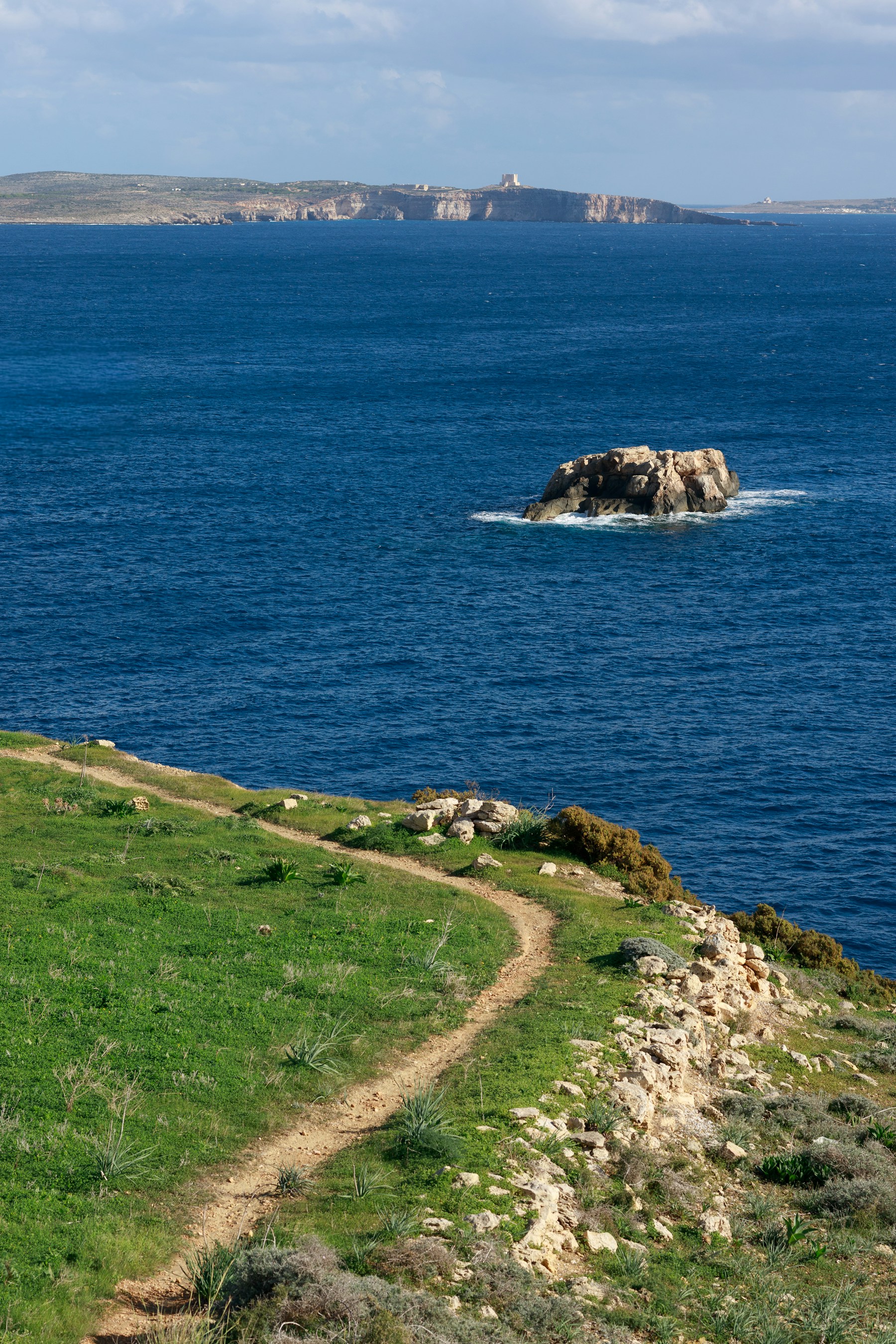 A narrow coastal path curving beside a brilliant blue sea