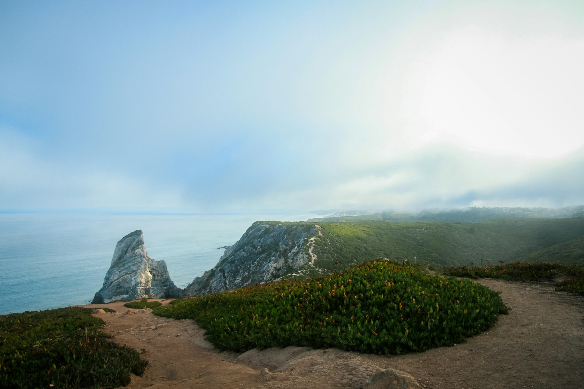 Fog lifting over green cliffs and the Atlantic at Praia da Ursa
