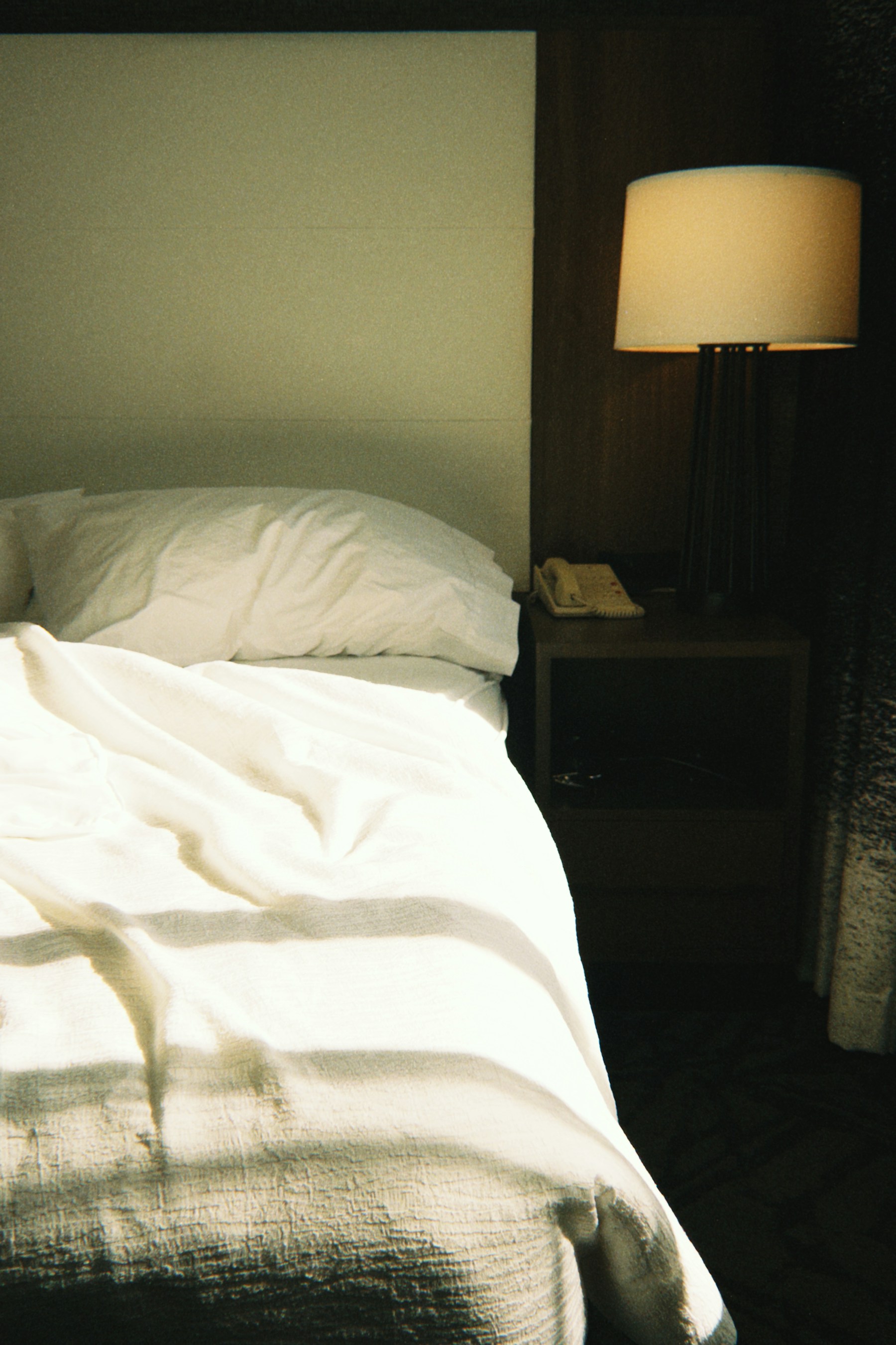 Morning sun and shadow crossing an unmade white bed