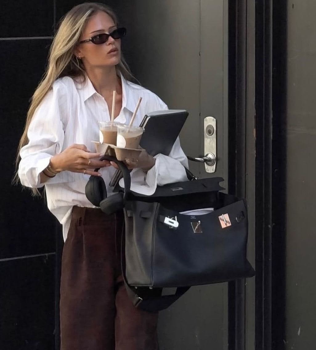 Woman carrying drinks, a tablet and a large work bag